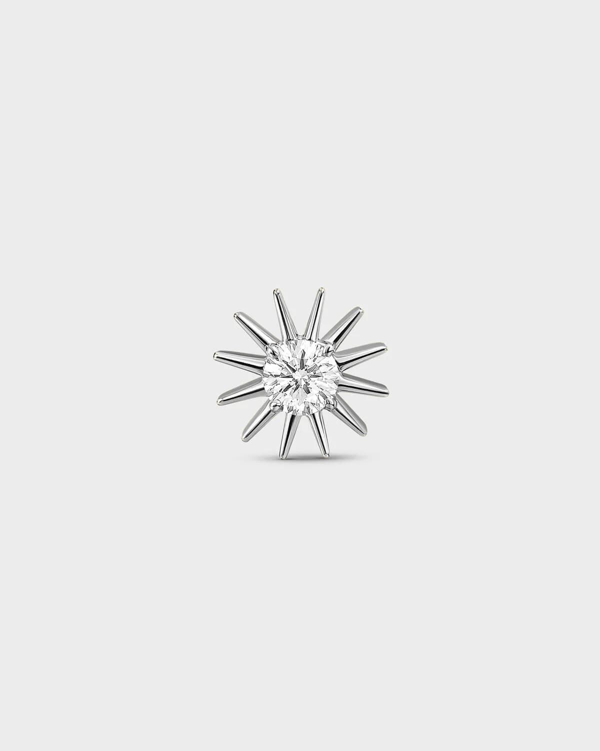 Polished silver Titanium threadless end earring with a round-cut clear stone set within a sculpted starburst design. On a light grey background.