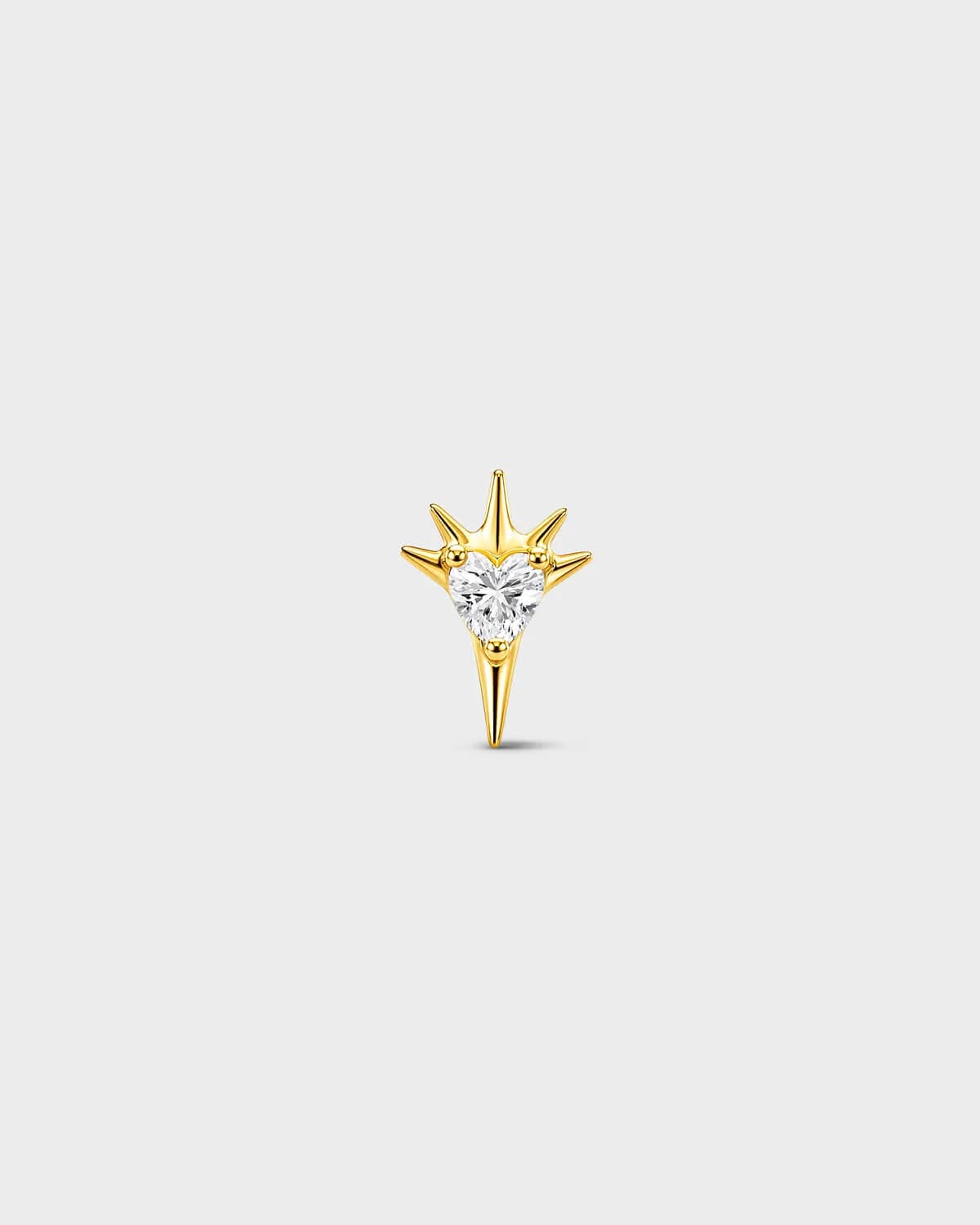 Gold titanium threadless end earring with a heart-cut clear stone set within a sculpted starburst design. On a light grey background.